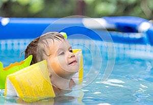 Kid in oversleeves swims in the pool in the yard