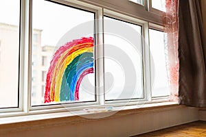 Kid painted rainbow during Covid-19 quarantine at home. Girl near window. Stay at home Social media campaign for coronavirus