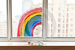 Kid painted rainbow during Covid-19 quarantine at home. Girl near window. Stay at home Social media campaign for coronavirus photo
