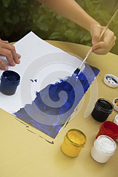 Kid painting a blue stroke of the paint brush isolated on white. Education and school.