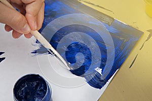 Kid painting a blue stroke of the paint brush isolated on white. Education and school.