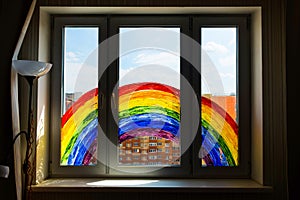 Kid painting rainbow during Covid-19 quarantine at home. Girl near window. Stay at home Social media campaign for