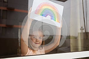 Kid painting rainbow during Covid-19 quarantine at home. Girl near window. Stay at home Social media campaign for coronavirus