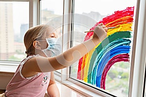 Kid painting rainbow during Covid-19 quarantine at home. Girl near window. Stay at home Social media campaign for coronavirus