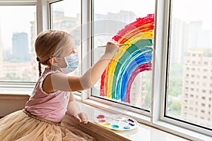 Kid painting rainbow during Covid-19 quarantine at home. Girl near window. Stay at home Social media campaign for coronavirus