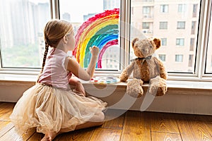 Kid painting rainbow during Covid-19 quarantine at home. Girl near window. Stay at home Social media campaign for coronavirus