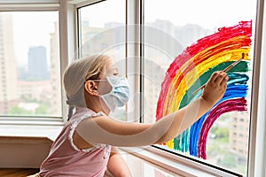 Kid painting rainbow during Covid-19 quarantine at home. Girl near window. Stay at home Social media campaign for coronavirus