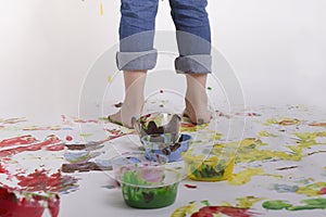 Kid paiting on the wall. Floor messy with different  colors