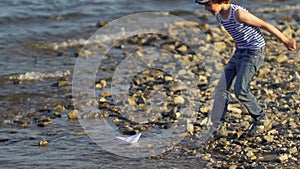 Kid with paper boat into water at beach. Little boy child puts paper ship on sea surface. ship sailing. Dreams, future