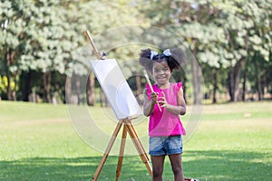 Kid in the park, Girl painting on the canvas in the park. Happy child girl drawing a picture outdoors