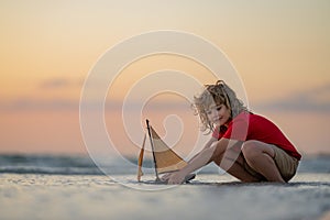 Kid play on the beach on a sunny day. Little sailor play with sailing boat in sea water. Child dreams of travel and