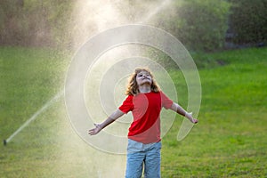 Kid play in garden. Child near automatic sprayers in garden. Watering in garden. Automatic lawn sprinkler watering grass