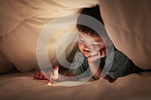 Kid play internet online game, under duvet.