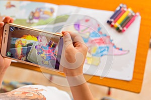 Kid playing Augmented Reality popup paintings of a filled dinosaur via mobile