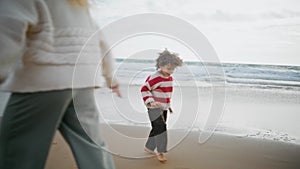 Kid playing autumn beach with parent on cloudy day. Barefoot curly boy resting