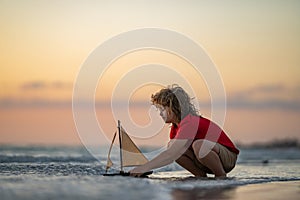Kid playing on the beach. Child play on the sea with toy ship boat. Little child having a happy moment play with toy