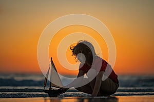 Kid playing on the beach. Child play on the sea with toy ship boat. Little child having a happy moment play with toy