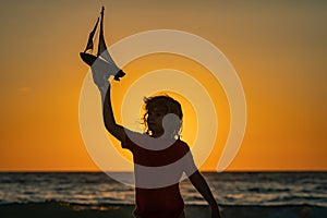 Kid playing on the beach. Kid playing with toy seailing boat on sunset sea. Little child having a happy moment play with