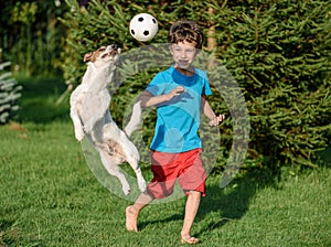 Kid playing football with family pet dog in backyard garden. Dog jumps to catch a ball