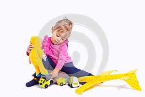 Kid playing indoor with toys on gray studio background. Blonde toddler little girl in kindergarten room play with