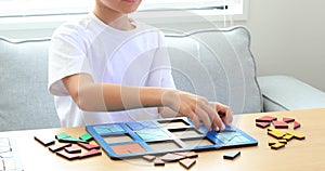 A kid is playing a logical wooden game on the table in the room. Educational toy
