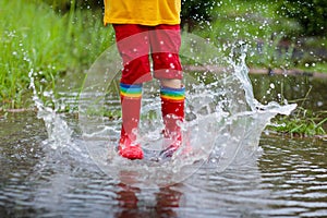 Kid playing out in the rain. Children with umbrella and rain boots play outdoors in heavy rain. Little boy jumping in muddy puddle