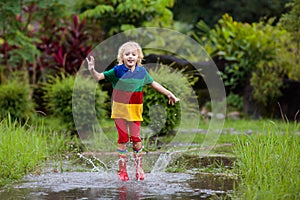 Kid playing out in the rain. Children with umbrella and rain boots play outdoors in heavy rain. Little boy jumping in muddy puddle