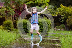 Kid playing out in the rain. Children with umbrella and rain boots play outdoors in heavy rain. Little boy jumping in muddy puddle