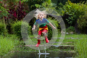 Kid playing out in the rain. Children with umbrella and rain boots play outdoors in heavy rain. Little boy jumping in muddy puddle photo