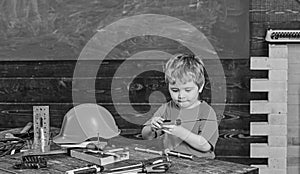 Kid playing with red screwdriver. Small boy in workshop. Tools lying on wooden table