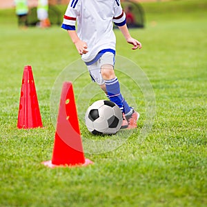 Kid playing soccer. Training football session for children. Boys is training with soccer ball and bollards on the field