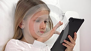 Kid playing tablet in bed, child browsing internet on touchscreen smartphone, girl portrait not sleeping relaxing on pc