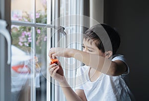 Kid playing with toy and looking at the midge climbing up outside of double glazed window. Boy sitting next to window looking out