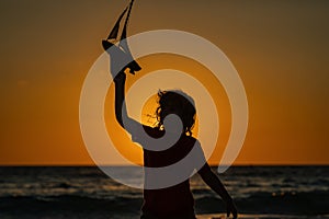 Kid playing with toy seailing boat on sunset sea. Travel and adventure concept. Child feeling adventurous while cruising