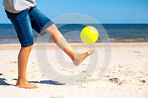 Kid playing with yellow beach ball on the sand by the sea water on a sunny day. Copy space for text. Vacation background