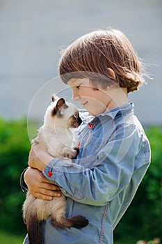 Kid plays in the summer outdoors. Ð¡hild is friends with pet in summertime. Cute toddler is playing with a kitten on grass. Boy