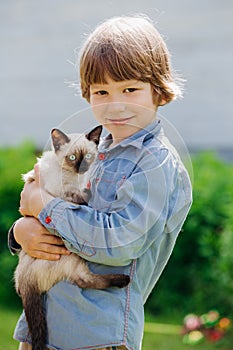 Kid plays in the summer outdoors. Ð¡hild is friends with pet in summertime. Cute toddler is playing with a kitten on grass. Boy