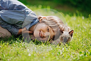 Kid plays in the summer outdoors. Ð¡hild is friends with pet in summertime. Cute toddler is playing with a kitten on grass. Boy