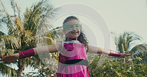 Kid plays a superhero outdoors, cute Child in a superhero costume, dressed in a pink cloak and a green hero mask, waving