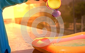 Kid plays water toys near poolside in swimming pool with sun light in summer vacation time