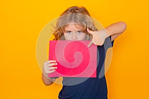 Kid pointing on empty sheet of paper, isolated on yellow background. Portrait of a kid holding a blank placard, poster