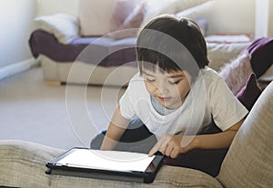 Kid pointing finger on Mock up tablet screen,Child boy lying on sofa relaxing at home watching cartoons or playing games on