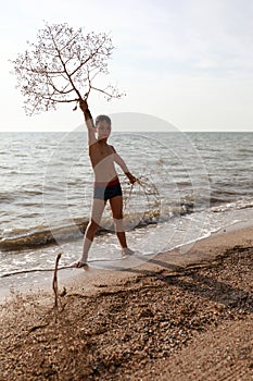 Kid posing with tumbleweed plant on beach of Azov sea