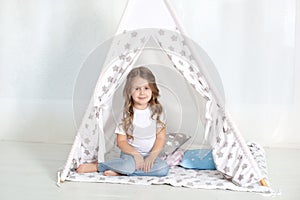 Kid prepare to go to bed. Pleasant time in cozy bedroom. A little girl sits in a tepee with colorful pillows in her room. Decorati