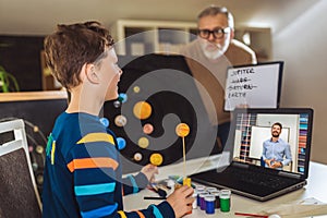 Kid presenting his science home project - the planets of our solar system. Father helping his son with online school lesson