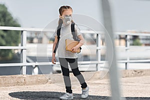 kid in protective mask walking with book on bridge air