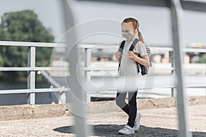 kid in protective mask walking with school bag on bridge air