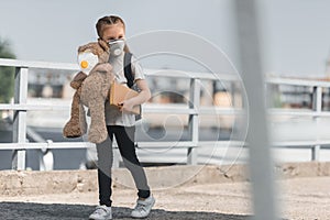 kid in protective mask walking with teddy bear and book on bridge air