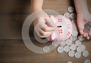 Kid put coin to piggy bank on the vintage wood background