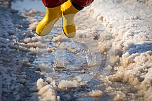 Kid in rainboots jumping in the ice puddle